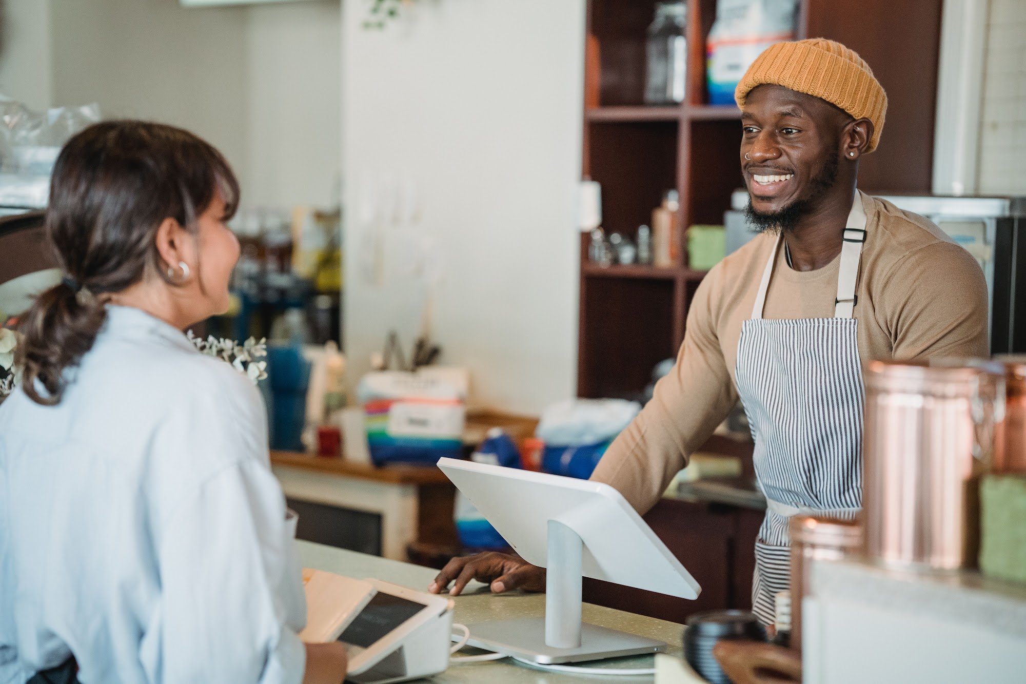 A smiling retail manager in a knitted hat at the checkout counter